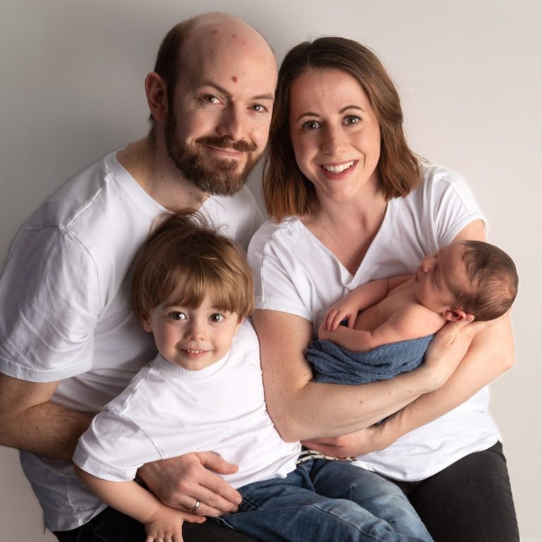A family of four, including parents and two young children, smiling together.